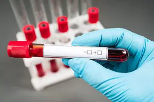 A gloved hand holds sample tube with a label. In the background are several more tubes in a rack. 