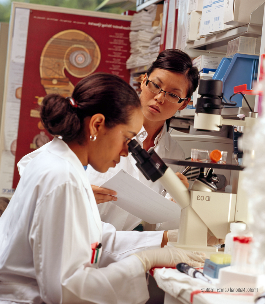 Woman researcher looking into microscope while another researcher looks on