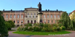 The image depicts a grand building at Uppsala University, showcasing classic architectural design. The edifice features a symmetrical façade with arched windows on the ground floor and rectangular windows on the upper floors, all framed with decorative moldings.
