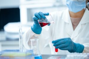 Researcher pouring a red liquid from a beaker to a test tube. 