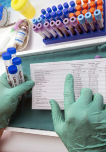 Gloved hands holding test tubes and a paper with test results. 