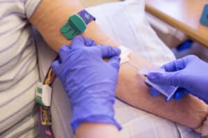 Close up of gloved hands drawing blood from a patient. 