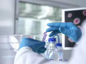 Gloved hands in a lab handling a sample vial. 