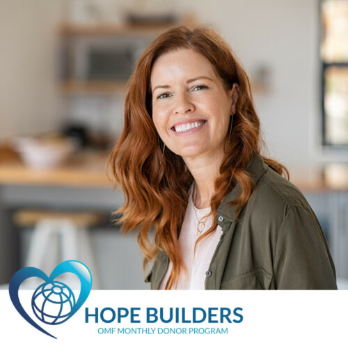 A smiling woman with shoulder-length reddish-brown hair, accompanied by the Hope Builders logo.