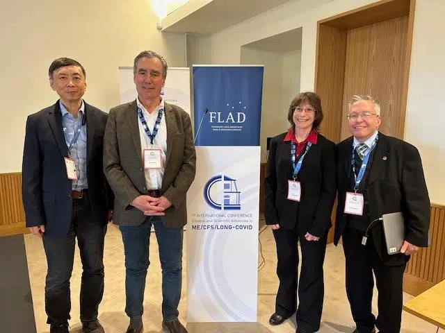 Picture of Linda Tannenbaum, Jonas Bergquist, David Systrom, and Wenzhong Xiao standing next to a banner for the 1st International Conference on ME/CFS and Long COVID in Portugal.