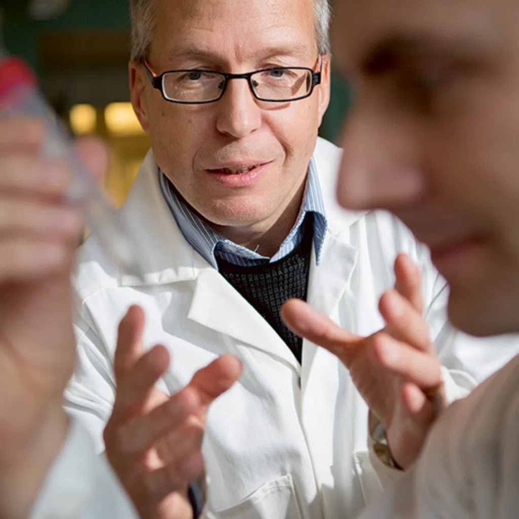 This image shows Jonas Bergquist in a lab. He is wearing glasses and a white lab coat. He is engaged in a discussion with one of his colleagues.