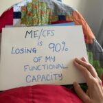 Bridie is holding a sign that reads: ME/CFS is losing 90% of my functional capacity.