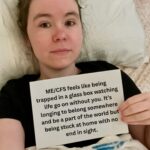 Hayden is holding a sign that reads: “ME/CFS feels like being trapped in a glass box watching life go on without you. It’s longing to belong somewhere and be a part of the world but being stuck at home with no end in sight.