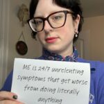 Katie is holding a sign that reads: “ME is 24/7 unrelenting symptoms that get worse from doing literally anything.”