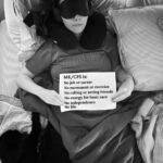 Lysh is holding a sign that reads: “ME.CFS is: No job or career, No movement or exercise, No calling or seeing friends, No energy for basic care, No independence, No life.