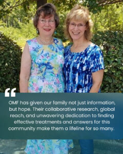 Vella and Amy standing close together outdoors in front of green trees and bushes. Below them is a testimonial text in a dark teal box: “OMF has given our family not just information, but hope. Their collaborative research, global reach, and unwavering dedication to finding effective treatments and answers for this community make them a lifeline for so many.”